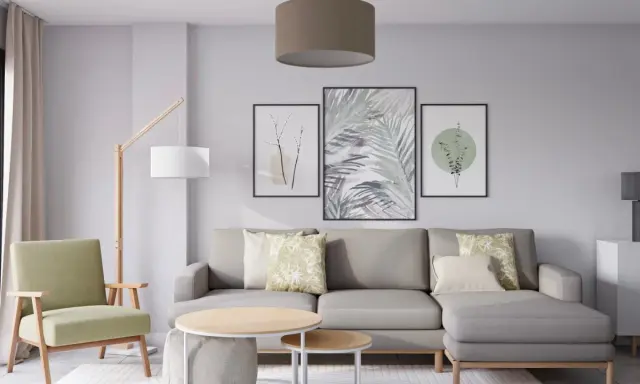Salón moderno con sofá gris, sillón verde y tres cuadros con motivos botánicos, mostrando diferentes formas de poner cuadros en la pared.