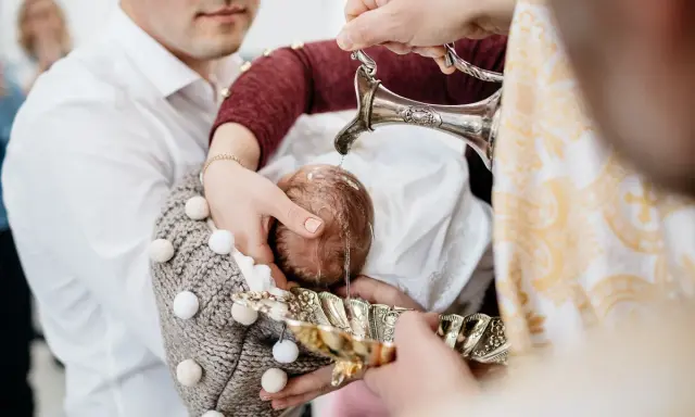 Woda święcona spływa na główkę dziecka podczas ceremonii na chrzcie.