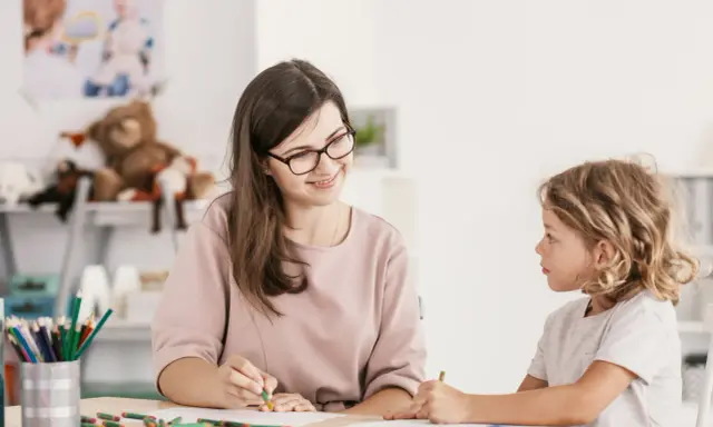 Bambina con ADHD, durante una sessione di diagnosi, disegna con una maestra sorridente.