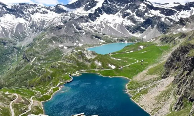 Laghi alpini blu e turchese ai piedi del Colle del Nivolet, con strade tortuose e montagne innevate sullo sfondo.