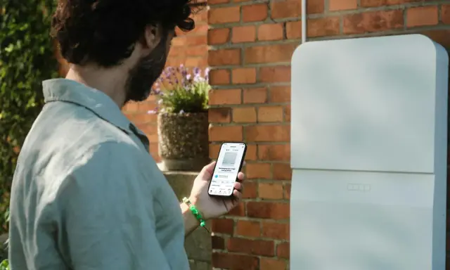 Man kollar sin mobil som visar information om sin batteribank hemma.
