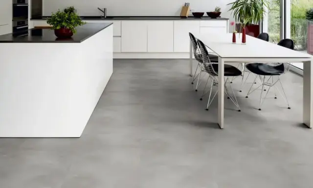 Cucina moderna con isola bianca e tavolo da pranzo. Il pavimento in LVT grigio effetto cemento completa l'ambiente minimalista.