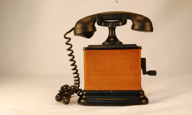 Stary telefon na korbkę z drewnianą obudową i czarną słuchawką.