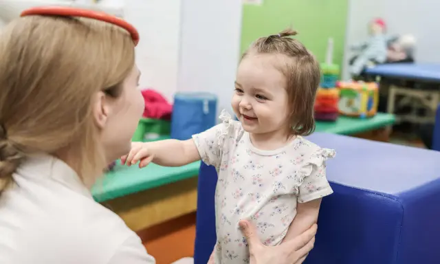 Uśmiechnięte dziecko wyciąga rączkę do terapeuty. To przykład, co to jest integracja sensoryczna – wspieranie rozwoju dziecka.