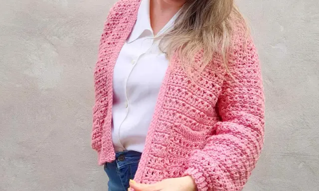 Mujer con un cardigan a crochet rosa, sobre una camisa blanca y jeans.
