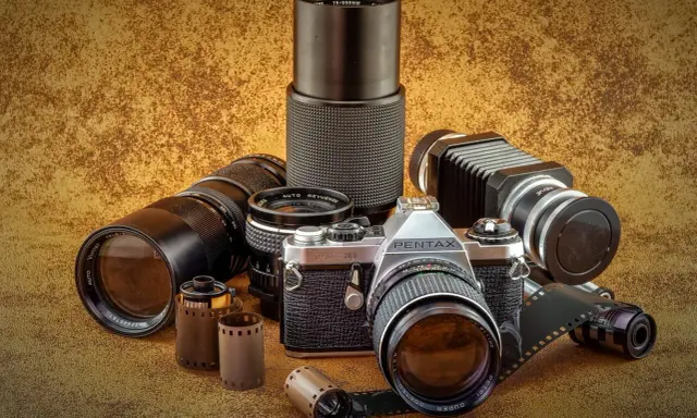 Kolekcja sprzętu fotograficznego: aparat Pentax JMC Super, obiektywy, mieszek i klisze.