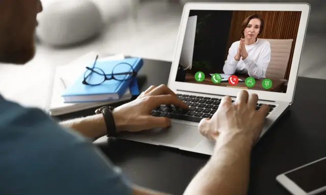 Mężczyzna prowadzi wirtualną superwizję przez laptopa. Na ekranie widać kobietę z dłońmi złożonymi w geście modlitwy.