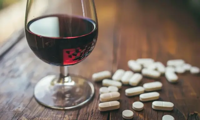 Kieliszek czerwonego wina obok garści tabletek. Leki przeciwzapalne a alkohol – potencjalne ryzyko interakcji.