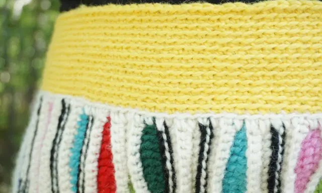 Detaljerad bild av en virkad kjol med gul resår och randigt mönster i vitt, rött, grönt, blått och rosa.