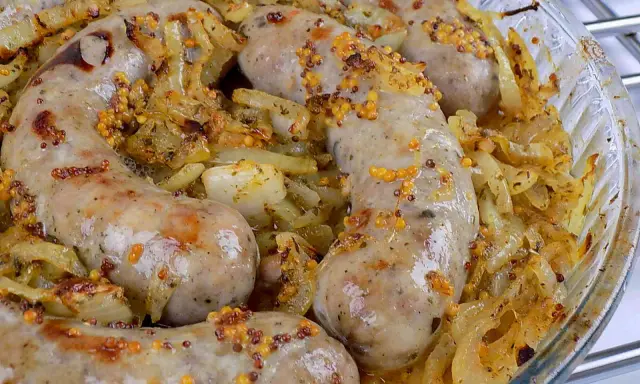 Biała kiełbasa surowa pieczona w piekarniku z cebulą i musztardą ziarnistą. Pyszne danie gotowe do podania.