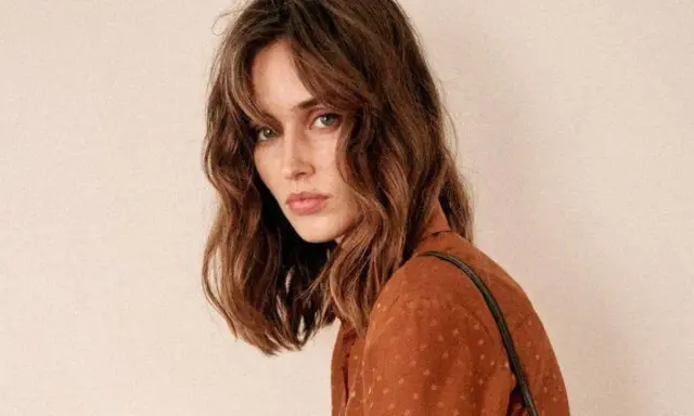 Mujer con un corte de pelo clavicut, ondas suaves y flequillo desfilado, luciendo un top marrón con lunares.