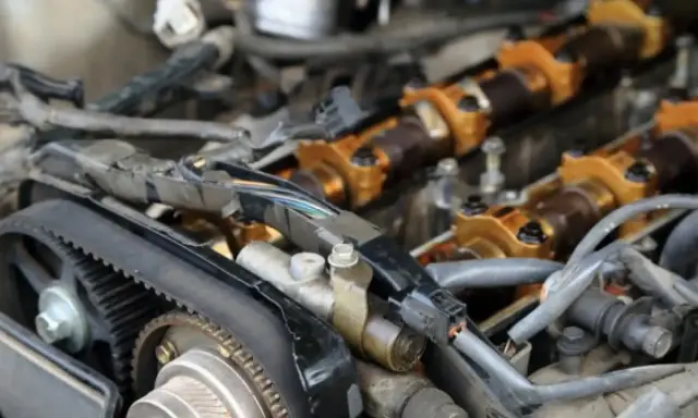 Motor de coche con correa de distribución y árbol de levas dorado. Se observa posible desgaste en el árbol de levas.