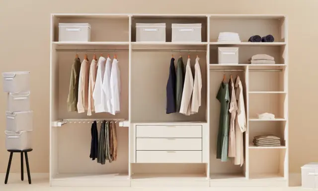 Ein aufgeräumter Kleiderschrank sortieren: Hemden, Hosen und Kleider hängen ordentlich an Kleiderbügeln. Stoffboxen und gefaltete Kleidung auf Regalen sorgen für Ordnung.