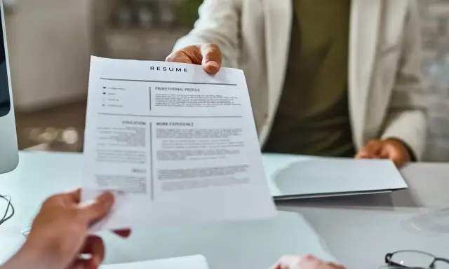 Osoba w jasnej marynarce podaje dokument CV.