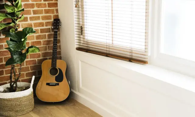 Gitara akustyczna obok ceglanej ściany i rośliny w koszu. Idealne miejsce na naukę piosenki na gitarę dla początkujących dzieci.