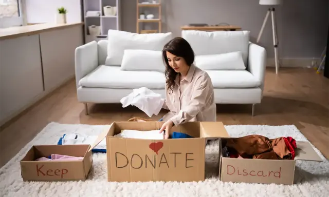 Donna fa decluttering, dividendo vestiti in scatole "Keep", "Donate" e "Discard".