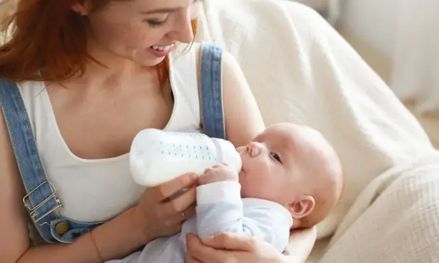 Mamma con capelli rossi nutre il suo neonato con latte artificiale ogni 2 ore. Il piccolo beve con gusto dalla bottiglia.
