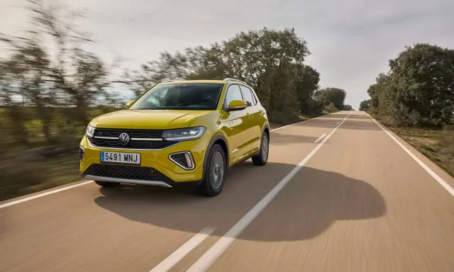 Un coche amarillo Volkswagen T-Cross circula por una carretera rural. ¿Cuánto se tarda en fabricar un coche? ¡Este parece listo para la carretera!