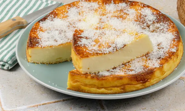 Un délicieux flan coco, saupoudré de noix de coco râpée, est servi sur une assiette. Une part est coupée et posée sur le dessus.