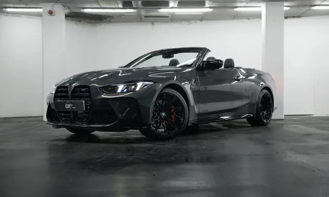 Un elegante BMW M4 negro descapotable, con sus luces LED encendidas, posa en un garaje.
