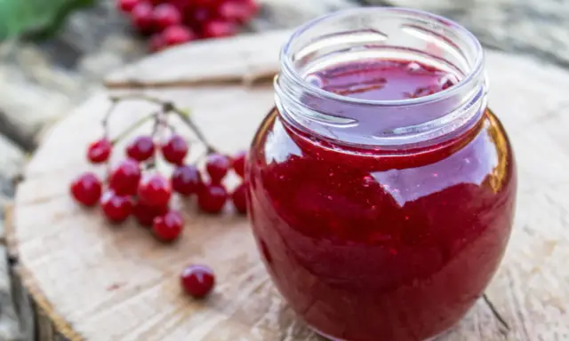 Un pot de gelee de groseille, aux reflets rubis, est posé sur une planche de bois. Des grappes de groseilles rouges sont disposées à côté.