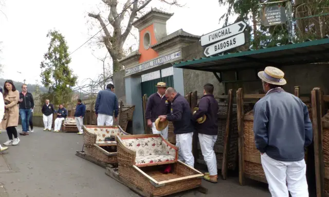 Korbschlitten Madeira: Männer in traditioneller Kleidung warten neben den Korbschlitten auf Fahrgäste.