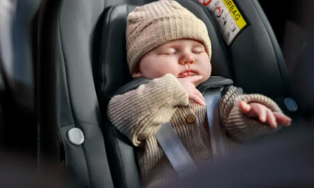 Śpiące dziecko w foteliku, bezpieczne dzięki 3 punktowym pasom bezpieczeństwa.