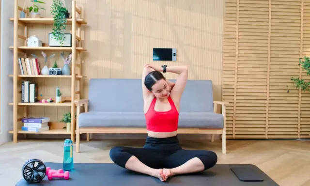 Frau dehnt sich im Schneidersitz, ein wichtiger Teil ihres Mobility Trainings. Trainingsmatte, Wasserflasche und Hanteln liegen bereit.