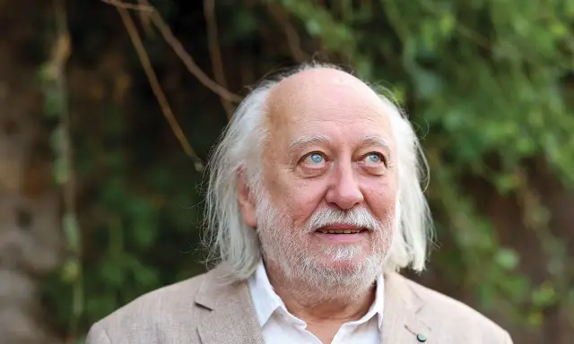 Ritratto di Laszlo Krasznahorkai, scrittore ungherese, con capelli bianchi e barba, sguardo pensieroso rivolto verso l'alto.