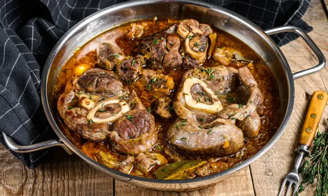 Ossobuco que es: jugosas rodajas de ternera cocinadas a fuego lento en una rica salsa con hierbas y especias, servidas en una sartén metálica.