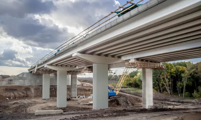 Construcción de un puente de viga con pilares de hormigón y grúa amarilla en el sitio.