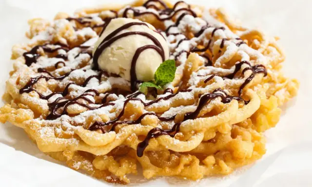 Pyszny funnel cake posypany cukrem pudrem, polany czekoladą i udekorowany gałką lodów waniliowych.