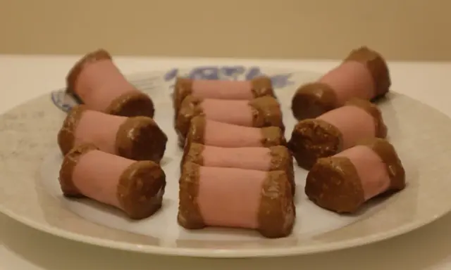 En tallrik med rosa marsipanbakelser doppade i choklad. Dessa små godsaker, som ser ut som en dammsugare i långpanna, är redo att avnjutas.