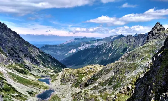 Majestatyczne Tatry Wysokie z doliną, dwoma stawami i skalistymi szczytami pod błękitnym niebem.