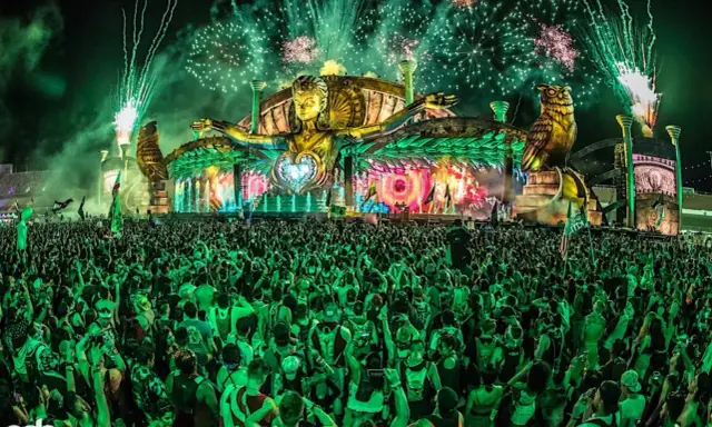 Folla immensa sotto un palco spettacolare con fuochi d'artificio verdi, uno dei rave party più famosi al mondo.