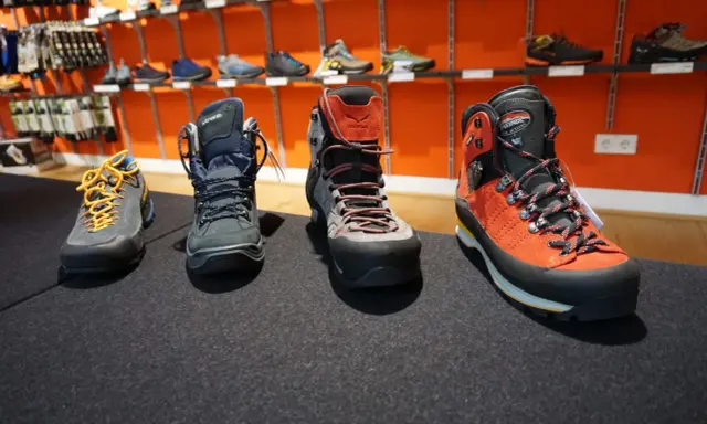 Vier Paar Wanderschuhe in verschiedenen Kategorien, von leichten Zustiegsschuhen bis zu robusten Bergstiefeln, stehen auf einem dunklen Teppich.