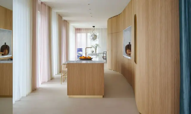 Interno moderno con isola cucina in legno e boiserie curvilinea. Tende leggere color pastello creano un'atmosfera soffusa.