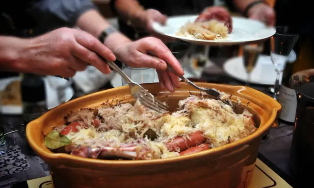 Un plat généreux de choucroute garnie, spécialité de la gastronomie alsacienne, est servi. Des mains servent ce délice, promesse d'une savoureuse nourriture d'Alsace.