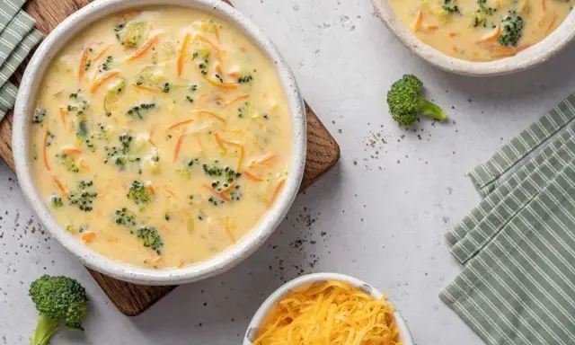 Un cremoso puré de brócoli y zanahoria, con trozos visibles de brócoli y ralladura de queso, servido en un cuenco blanco.