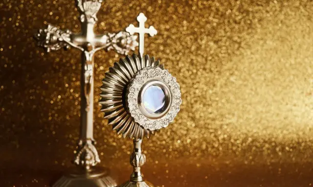 Monstrancja i krzyż na złotym tle. IHS to symbol Jezusa, który jest obecny w Eucharystii.