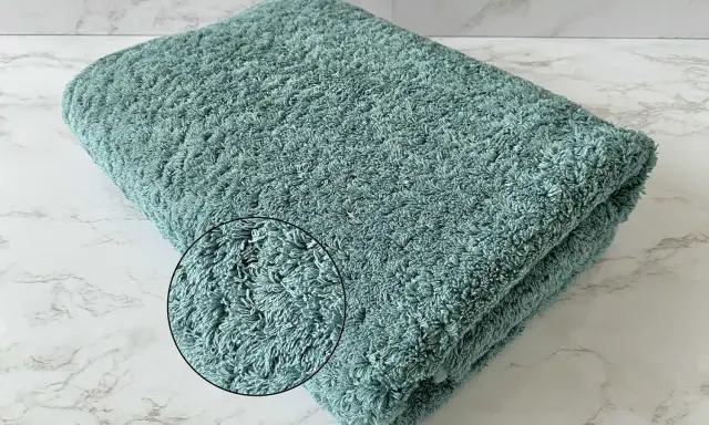 A folded teal terry cloth towel with a magnified inset showing its plush texture.