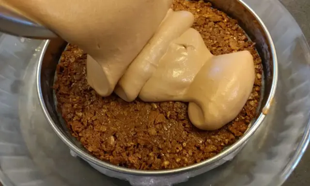 Une crème onctueuse est versée sur une base de croustillant praliné feuilletine dans un cercle à pâtisserie.