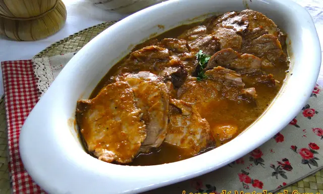 Arrosto di maiale morbido con sughetto, servito in una pirofila bianca, pronto per essere gustato.