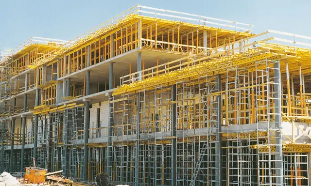 Edificio en construcción con intrincadas estructuras temporales amarillas y grises, sosteniendo los pisos de concreto.