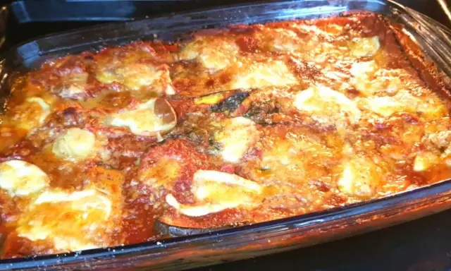 Parmigiana di melanzane appena sfornata, dorata e filante, in una teglia di vetro.