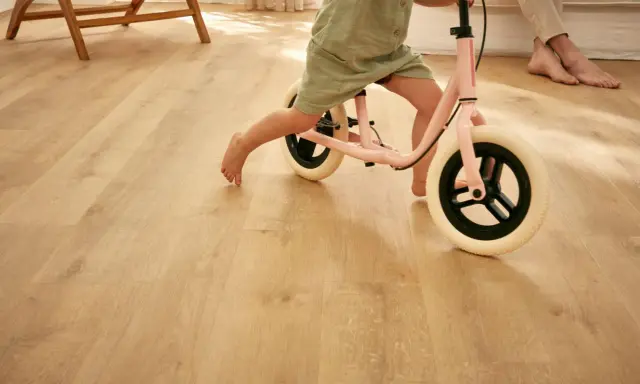 Un enfant apprend à faire du vélo d'équilibre sur un sol de salle de jeux en bois clair.