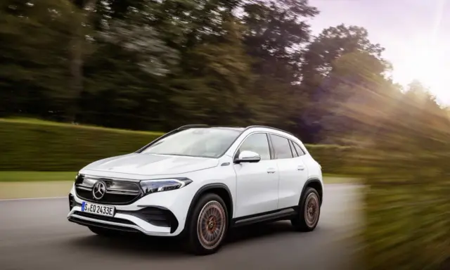 Un Mercedes EQA blanco circula por una carretera rodeada de árboles. Las **mercedes eqa medidas** son ideales para la ciudad y escapadas.