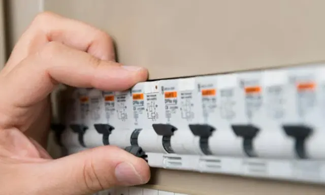 Main d'une personne actionnant un disjoncteur dans un tableau électrique. Les plombs ont sauté, il faut rétablir le courant.
