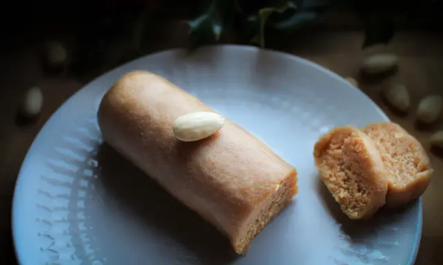 Un bâtonnet de pâte d'amande, garni d'une amande entière, repose sur une assiette blanche. À côté, deux tranches de ce délice, parfait pour un fond de tarte amande.