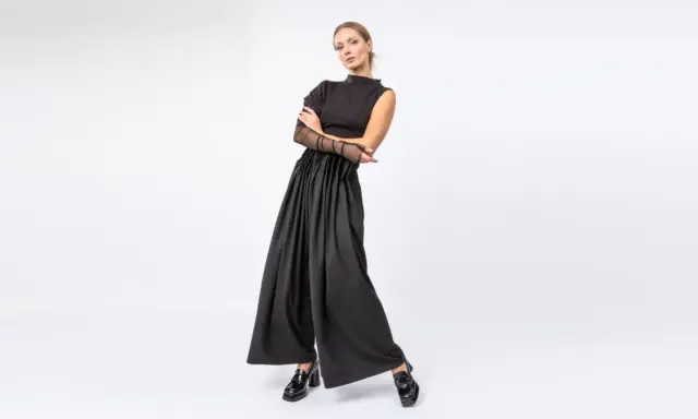 Elegancka kobieta w czarnych, szerokich spodniach i topie z siateczkowymi rękawami. Stylowe, lakierowane mokasyny to idealne buty do teatru.